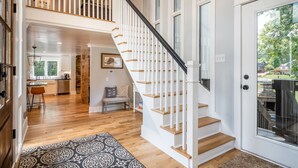 Un interior amplio con una escalera que lleva a un segundo piso, una zona de cocina y vistas al exterior.