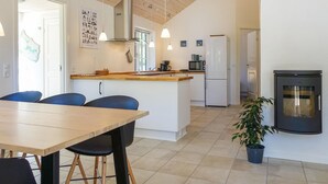 Una cocina moderna con una isla central, armarios blancos y un refrigerador negro. Hay dos lámparas colgantes, un microondas y una estufa.