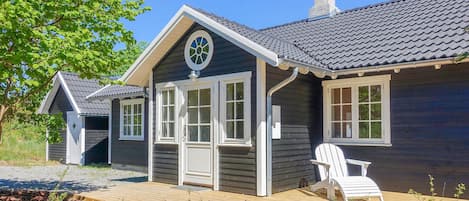 A wooden cabin with a gabled roof, a front porch, and a deck area with a chair.