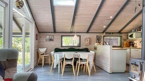 A cozy cabin interior with a dining area, wooden walls, a kitchen, and a large window.
