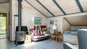 A cozy cabin interior with a wooden interior, a fireplace, a sofa, a table, and a bed.