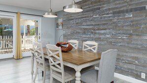 Een eetgedeelte met een houten tafel, witte stoelen en hanglampen.