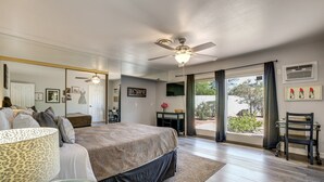 Een slaapkamer met een bed, een plafondventilator, een groot raam en uitzicht op de omgeving.