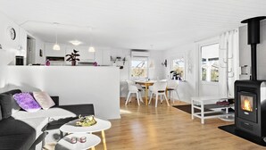 A modern, well-lit living room with a sofa, coffee table, and a fireplace. A kitchen area with a dining table and chairs is visible in the background. - Amazing home in Haderslev with WiFi (Haderslev)