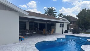 Ein Garten mit Swimmingpool, Terrassenmöbeln und einem überdachten Essbereich im Freien.