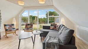 A spacious room with a large window, a sofa, a small table, and a chair. - 5 bedroom nice home in Hadsund (Hadsund)
