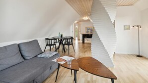 A modern living room with a grey sofa, a wooden coffee table, and a unique white spiral staircase. - 5 bedroom nice home in Hadsund (Hadsund)