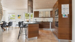 A modern kitchen with a central island, bar stools, and a dining area with a view of greenery. - 5 bedroom nice home in Hadsund (Hadsund)