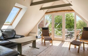 Relax in a peaceful attic retreat with a panoramic view of the surrounding greenery, featuring a comfortable sofa and seating area.