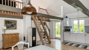 A spacious kitchen with a wooden staircase, a dining area with a table and chairs, and a view of greenery outside.