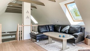 A modern loft bedroom with a sloped ceiling, a black leather sofa, a small table, and a skylight.