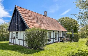 Traditional house with a steeply pitched roof and chimney, surrounded by a well-manicured lawn and lush greenery, offering a grill for outdoor cooking.