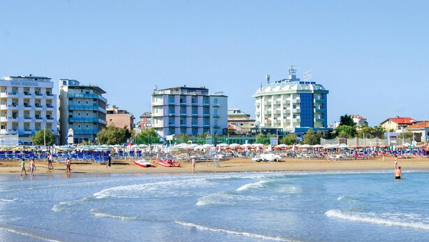 Een strand met verschillende gebouwen op de achtergrond, waaronder een hotel met een blauw-witte gevel.