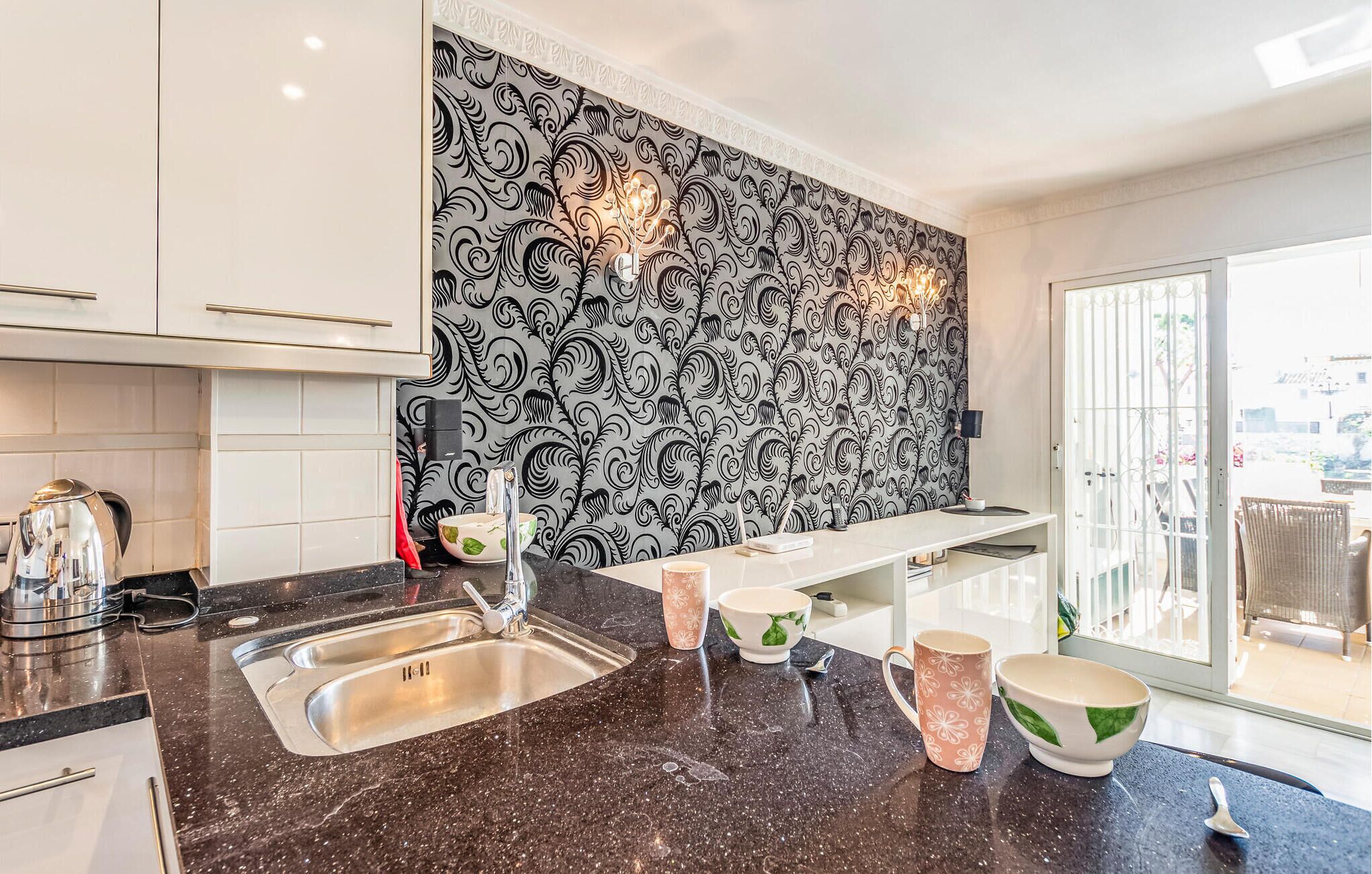 A modern kitchen with a black and white patterned backsplash, stainless steel appliances, and a large window providing natural light.