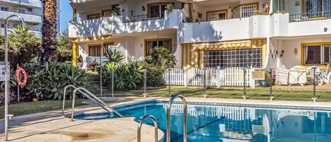 A swimming pool with a white fence, palm trees, and a building with balconies.