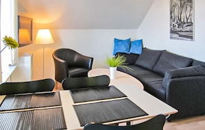 Een moderne woonkamer met een zwarte leren bank, een ronde salontafel en een kleine potplant.