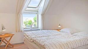 Un dormitorio con tragaluz, dos mesitas de noche con lámparas, una cama con edredón estampado y una ventana con planta en maceta.