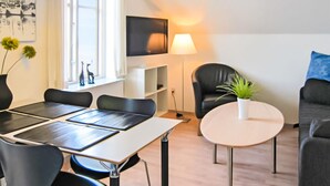 Una sala de estar moderna con comedor, que incluye un sofá, una mesa de centro y un televisor montado en la pared.