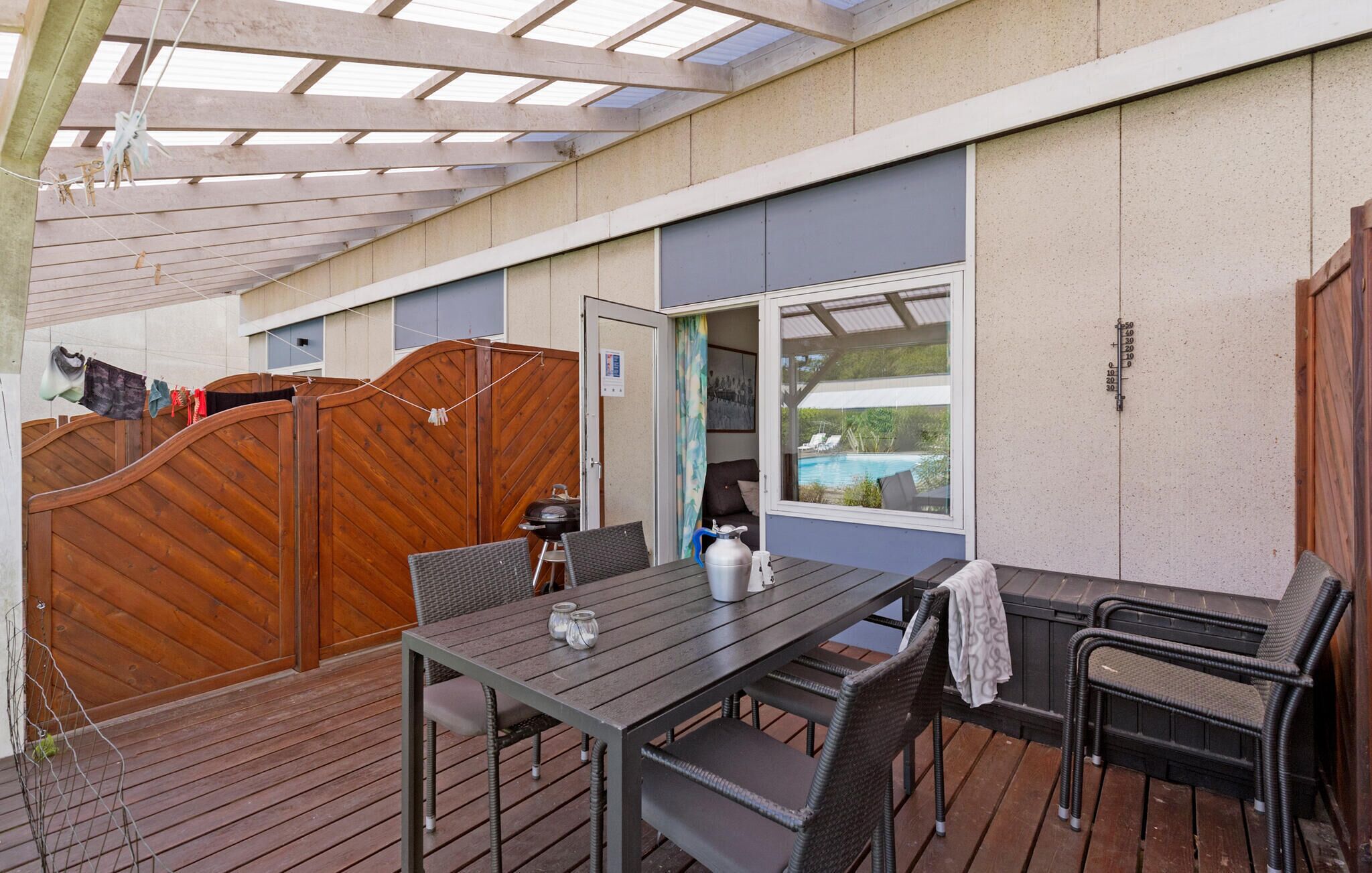 Un patio al aire libre con mesa y sillas de madera, una parrilla y vistas a una piscina.