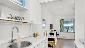 A modern kitchen with a stainless steel sink, white cabinetry, and a wooden dining table. - Awesome apartment in Nexø with sauna (Nexø)