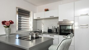 Une cuisine moderne avec des meubles blancs, un four encastré, une cuisinière et une bouilloire.
