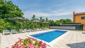 Une piscine entourée de verdure et d’un bâtiment, avec des chaises longues et des parasols.