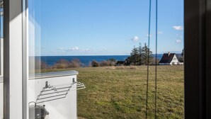 Vista desde el interior de un edificio hacia un campo de césped y una casa al otro lado del agua.