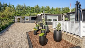 A modern house with a gravel driveway, surrounded by a wooden fence and a variety of potted plants. - Awesome home in Sjølund with WiFi (Sjølund)