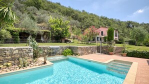 A swimming pool with a stone border, surrounded by a garden with various plants and a stone wall. - Gorgeous home in Prelà (Prelà)