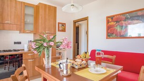 Eine gemütliche Küche mit Holzschränken, einem Esstisch mit Kaffeemaschine, einer Obstschale und einem roten Sofa.