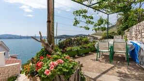 Eine Terrasse mit Meerblick, einer Steinmauer und einem Tisch mit Stühlen.