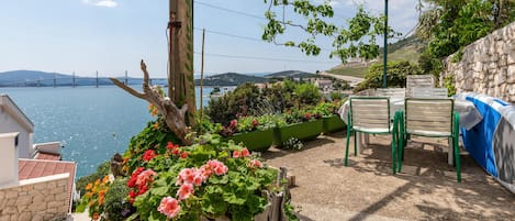 A terrace with a view of the sea, a stone wall, and a table with chairs.