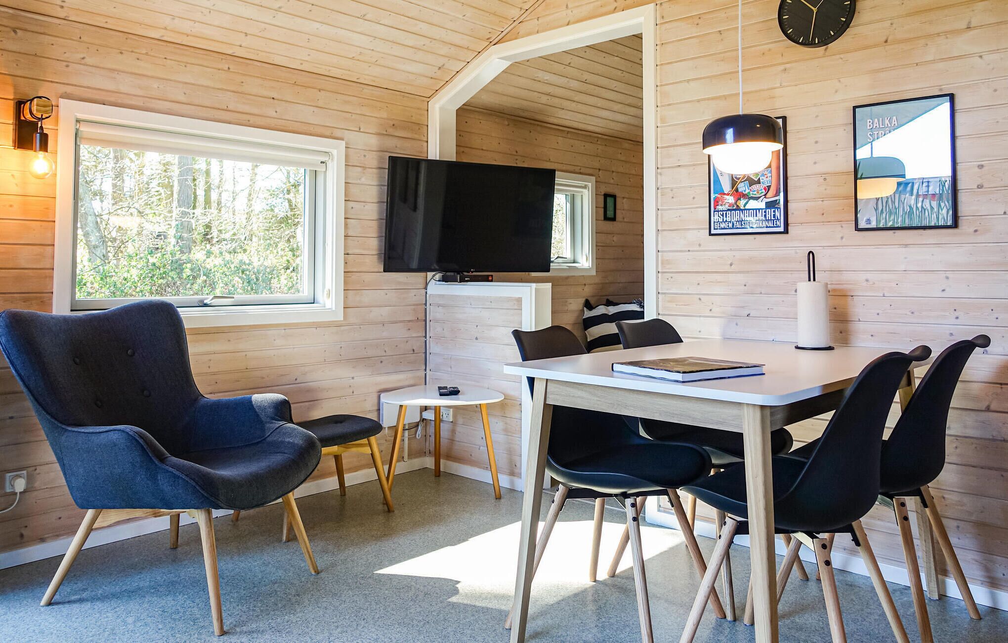 A cozy room with a wooden interior, a TV mounted on the wall, a dining table with chairs, and a window providing natural light.