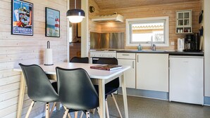 Eine kleine Küche mit Holzwänden, einem Esstisch mit Stühlen, einem Herd und einem Fenster mit Jalousien.