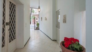 A hallway with a tiled floor, a door with a diamond-patterned window, a hanging light fixture, and a potted plant with red flowers.
