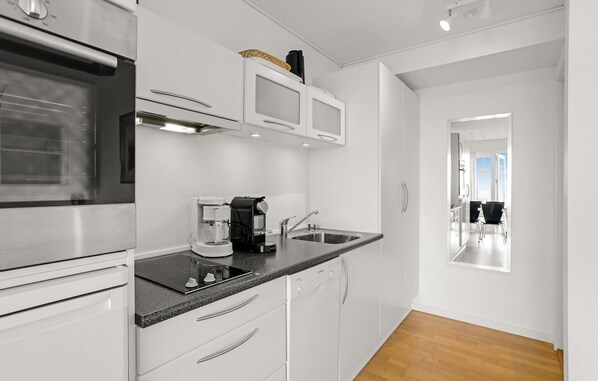 Una cocina moderna con armarios blancos, horno integrado, cafetera y lavabo.