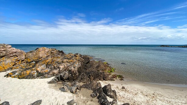 En klippig kustlinje med klart blått vatten och en sandstrand.