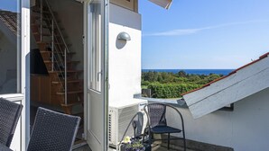 En balkong med utsikt över havet, en stol, ett litet bord med en blomma och en trappa som leder in.