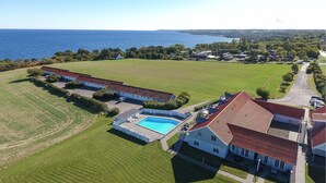 En vy från ovan av en fastighet med en swimmingpool, en stor gräsmatta och utsikt över havet.