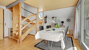 Ein Essbereich mit einer Holztreppe, einem Esstisch mit Stühlen, einer Uhr und einem Fenster mit Vorhängen.