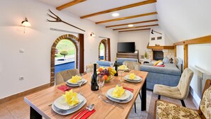 A dining area with a wooden table set for four, a sofa, and a TV in the background. - Nice home in Ljubescica with sauna (Ljubescica)
