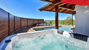 A hot tub with a wooden deck and lounge chairs, overlooking a pool and scenic landscape. - Nice home in Ljubescica with sauna (Ljubescica)