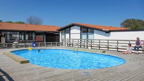 Een zwembad met houten terras, een gebouw met rode dakpannen en een omheining.