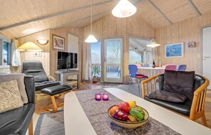 Un salon chaleureux avec un téléviseur, des sièges confortables, un coin repas et une vue à travers une porte vitrée.
