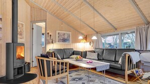 A cozy cabin interior with a fireplace, wooden walls, a sofa, a table, and a window with a view of trees. - Stunning home in Sydals with sauna (Sydals)