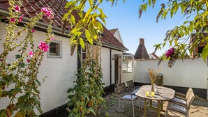 A white house with a tiled roof, a chimney, and a garden with flowering plants. - 1 bedroom awesome home in Svaneke (Svaneke)
