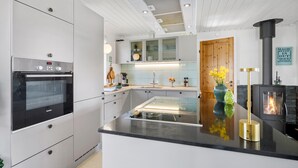Una cocina moderna con horno empotrado, una isla central con encimera de vidrio y una estufa a leña.