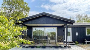 Una casa moderna con un porche cubierto, grandes puertas de cristal y un jardín cuidado.