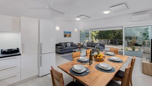 A modern kitchen with white cabinets, a dining area with a wooden table set for four, and a living area with a grey sofa and a painting on the wall. - Stunning home in Zestilac (Zestilac)