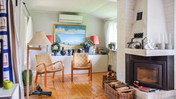 Un salon chaleureux avec une cheminée, deux fauteuils en osier, un plancher en bois et un tableau accroché au mur.